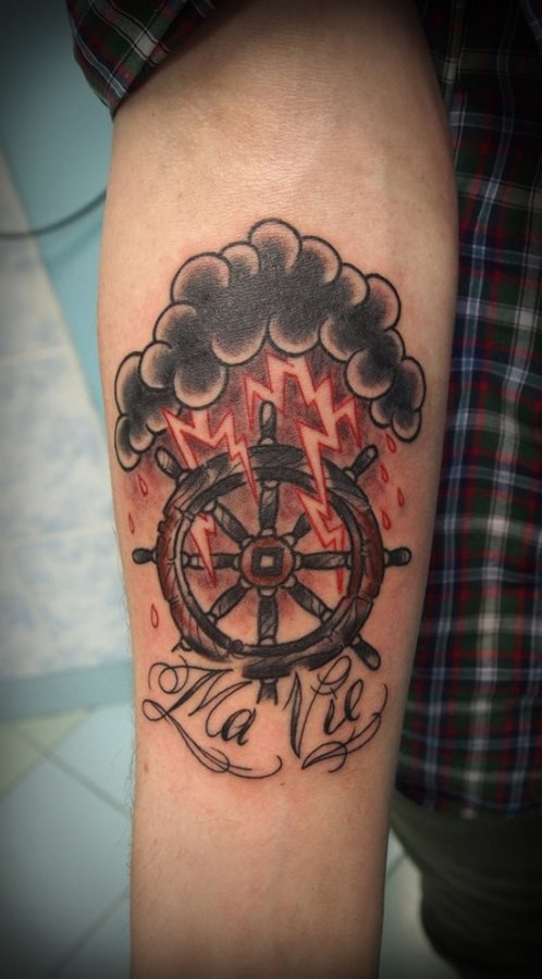 Tatuaje de un timón de un barco en el biceps de este chico, con rayos de color rojo simulando tormenta. Tiene una inscripción que puede referirse a un significado especial para la persona.
