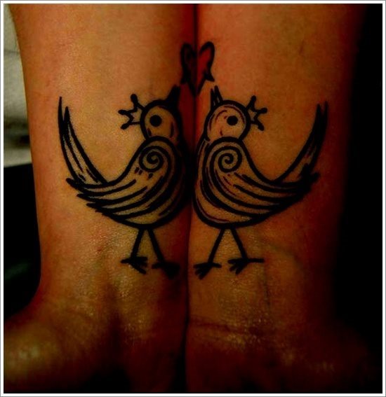 Tatuaje de pareja formado por dos pájaros iguales con una pequeña cresta, que parece una corona y en la parte superior se ha tatuado un corazón que necesita la pareja unir sus brazos para que sea vea el corazón al completo