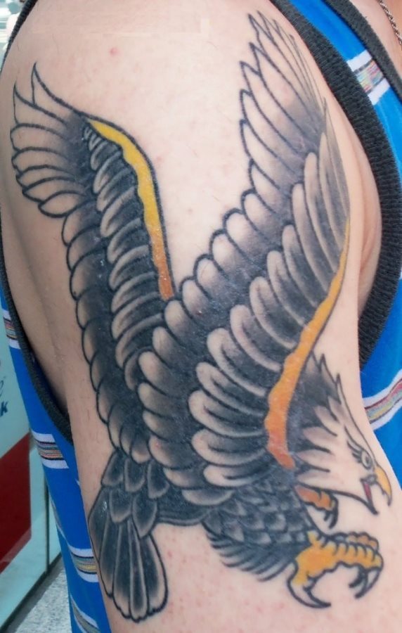 Tatuaje de un guila en tons negros con detalles en color naranja como se puede observar en el pico, las patas y los lados de las alas