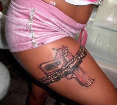 Tatuaje de un arma sujeta por un liguero que lleva una chica tatuado sobre su muslo