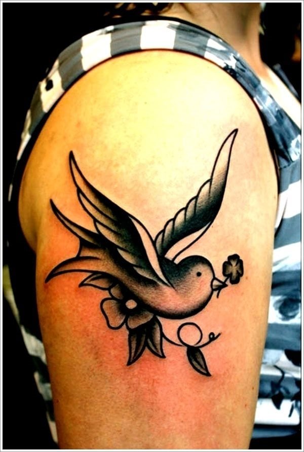 Tatuaje de una golondrina de gran tamaño a color negro sobre el brazo, que lleva sobre su boca una pequeña flor, un trabajo muy bien rematado gracias a definir muy bien la silueta del pájaro y conseguir un difuminado muy acertado en las alas
