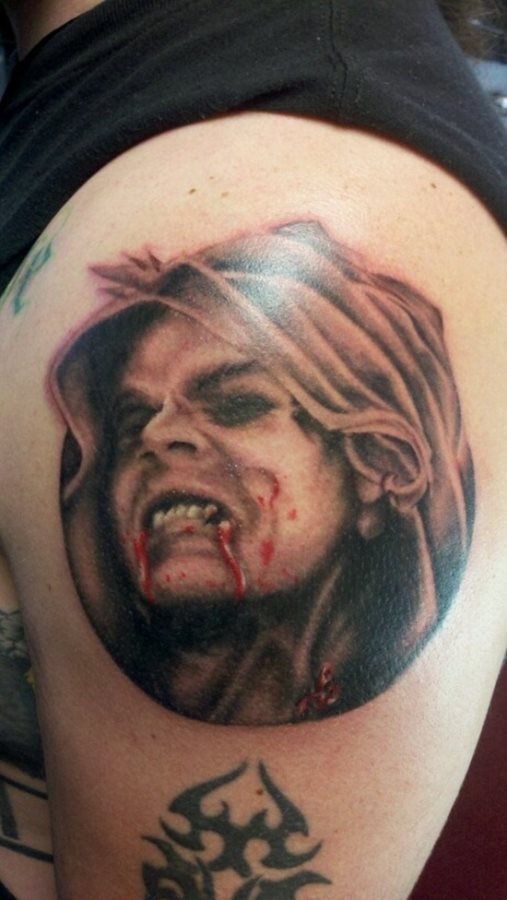 Tatuaje de un vampiro con capucha en el que destacan los enormes colmillos de los que brotan restos de sangre, un tatuaje un tanto satáico en el que las facciones conseguidas con las arrugas de la cara es el detalle más sobresaliente de este tuaje