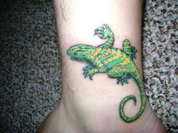 Tatuaje de un reptil en tonos verdosos y amarillos en el tobillo