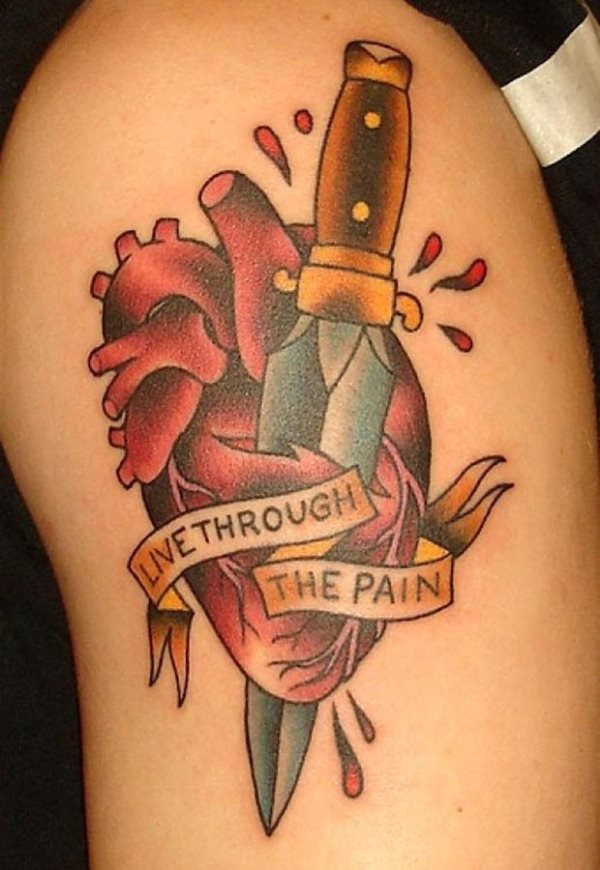 Tatuaje a color de un cuchillo que se ha clavado en el corazón y brotan de él algunas gotas de sangre, en medio del tatuaje se ha dejado escrito a través de un lazo que recorre todo el corazón la frase 
