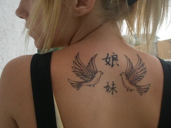 El siguiente tatuaje es de un par de pjaros cara a cara que revolotean junto a dos caracteres chinos