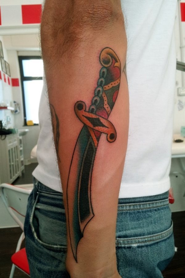 Tatuaje de un cuchillo tipo árabe, por la curvatura que se le ha dado a la hoja y las formas del mango, realizado a colores verdes, amarillos y rojos, que se han tataudo en el antebrazo de un hombre, la verdad es que ha quedado un tatuaje bonito, a pesar de que nosotros somos más de tatuajes de paz