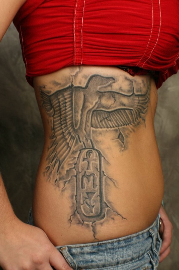 No es fcil describir alguno de los tatuajes que vemos en esta galera en los cuerpos de algunas personas porque yo no soy un experto en el mundo egipcio as que en este caso solo puedo decir que se trata de un diseo en el costado que parece un guila y que tiene un smbolo desconocido para mi en el parte inferior