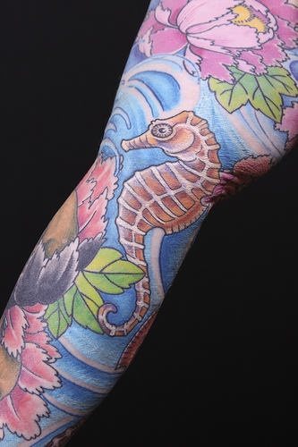 Tattoo con varios motivos floreados y un caballito de mar que cubre toda la pierna