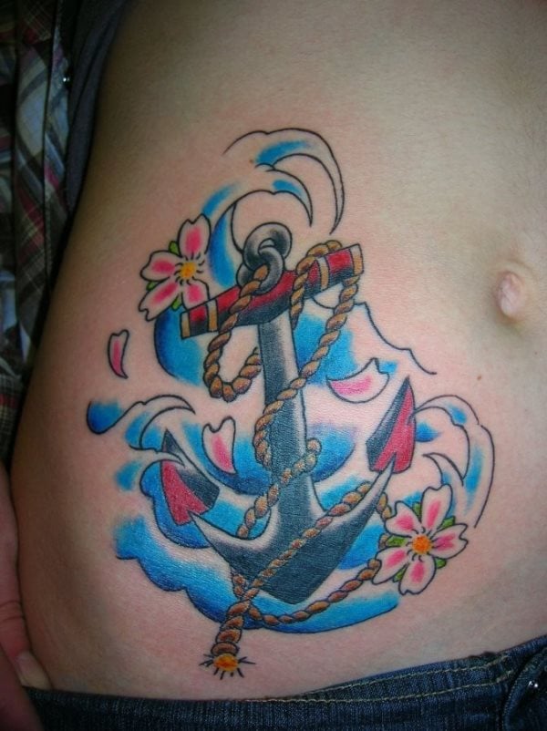 Ahora vemos un tatuaje situado prximo al ombligo de un ancla sobre unas olas, rodeado de unas flores de cerezo que flotan