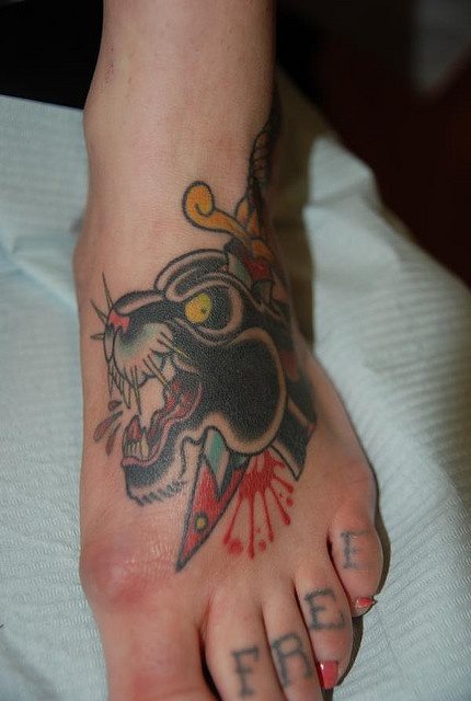 La cabeza de esta pantera est atravesada por una daga, tatuada en el empeine y la palabra FREE sobre los dedos del pie