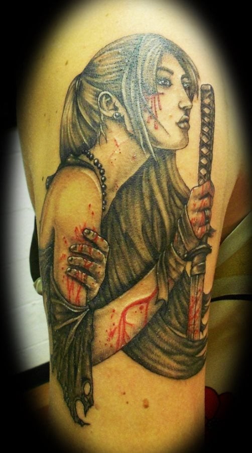 Tatuaje de una chica que lleva una espada samurai con restos de sangre en sus manos, brazos y cara