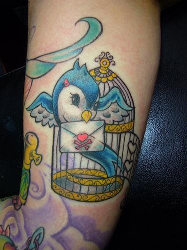 Original tatuaje y muy colorido de un ave que sale de su jaula