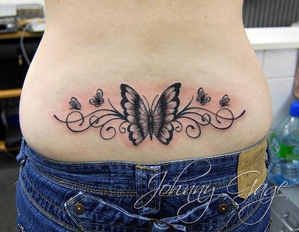 Mariposa reresentada en tonos negros en la parte inferior de la espalda acompaada por otras mariposas ms pequeas