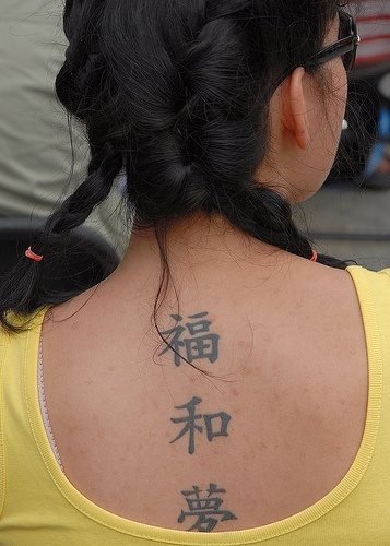 Aqu tenemos este tatuaje en tinta negra de tres caracteres chinos situados verticalmente nuevamente en el centro de la espalda de esta chica