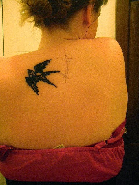 Pequeo tatuaje de una golondrina tatuada en la parte superior de la espalda, justo debajo de la nuca