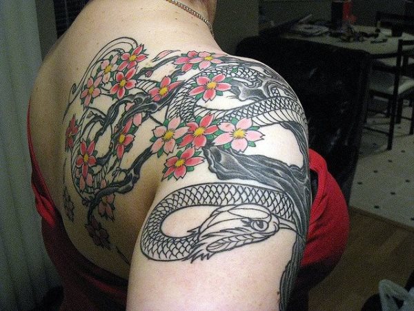 En este tatuaje la serpiente est hecha de tinta negra, el toque de color lo dan las flores de cerezo rosadas