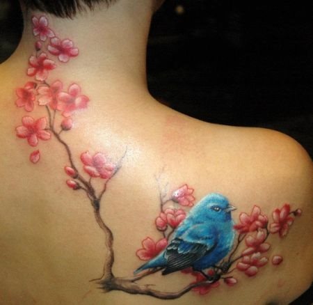 Este colorido tatuaje por el que ha optado esta chica es de unas ramas de flores de cerezo con un bonito pjaro azul que se posa sobre una de ellas