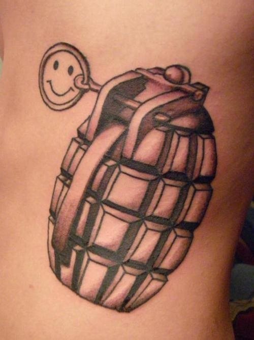 Tatuaje de una granada muy realista a color negro y en cuyo centro de la anilla se ha tatuado la clásica sonrisa