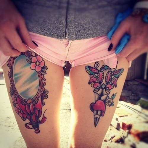 Tatuaje muy femenino en las piernas, en una de ellas se ha tatuado un espejo clásico con grandes adornos, lazos y flores y en la otra pierna, parece una aguja con mariposas que se ha clavado en un corazón
