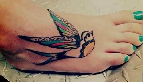 Tattoo en el empeine de una golondrina a la que se le dan toques de color en las alas del ave
