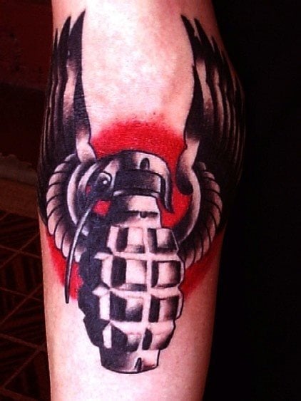 Tatuaje de una granada de gran tamaño, al que le acompañana dos alas que parecen forma parte de la propia granda, de fondo se ha tatuado un sombreado rojo que hace destacar los elementos y componentes de esta granada