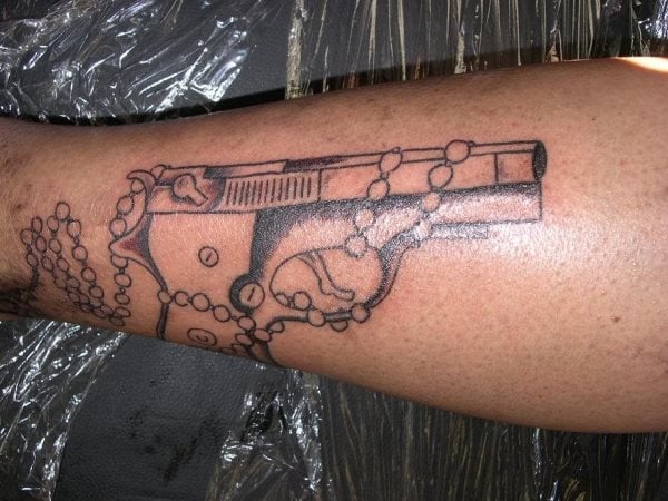 Tatuaje de una pistola envuelta por un rosario, un tattoo muy típico de algunos países del sur de América, sobre todo por personas que pertenecen a algunas bandas o mafias y que se hacen este tipo de tatuajes cuando han cometido algún acto delictivo en el que se han utilizado armas