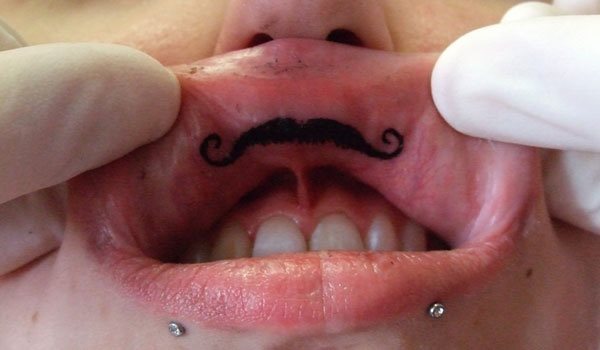 Diseo de un bigote en el interior del labio, concretamente en la zona superior, de manera que cuando se muestra parece el bigote bajo la nariz; esto nos hace ver que es una zona estratgica y ms que pensada para tatuarse este diseo