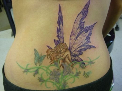 Tatuaje de un duende alado en la cintura, tatuaje del que destacamos el acertado colorido para el plumaje de las alas y las hojas que van recorriendo bajo el duende con unas florecillas y mariposas, tal vez el aspecto de tribal del ramillete no sea el que más nos guste