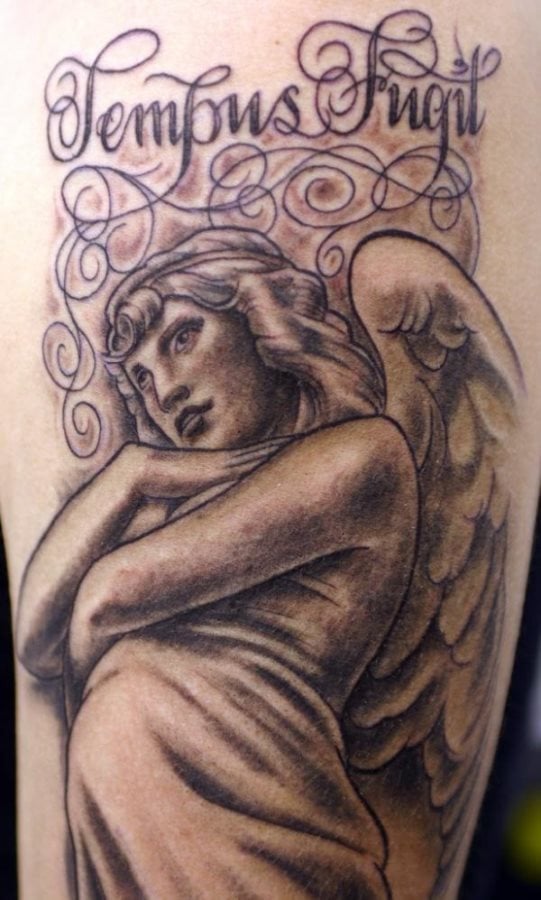 Tatuaje de un ángel alado de largo cabello rizado, que ha sido rodeando de unas finas cenefas formando bonitos garabatos y en cuya parte superior del tatuaje se han escrito las palabras Tempus Angil