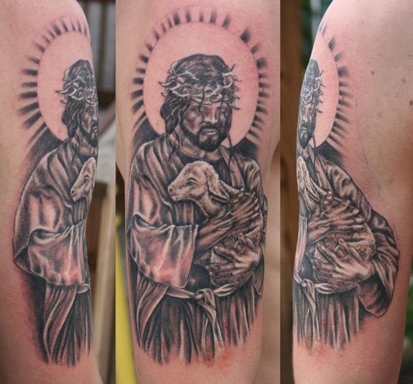 Tatuaje del hijo de Dios con corona de espinas, una corona de halo muy espiritual y una gran túnica con grandes sombreados, además lleva sobre sus brazos un pequeño cordero