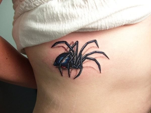 Tatuaje de una pequeña araña sobre el costado de una mujer, en esta ocasión nos encontramos ante una araña de largas patas y cuerpo negro, que seguro dará algo de miedo a algunas personas cuando la vean