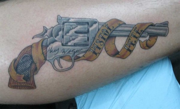 Tatuaje de un wevolver del tipo de películas western, al que rodea un alzo azule con acabados agrietados y las palabras pistol pete, al igual que podemos apreciar ocmo en la pistola se han serigrafiado también algunas palabras que no podemos apreciar con claridad, otro tatuaje de malote