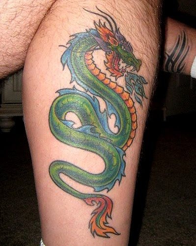 Tatuaje de un dragón en la pierna que expulsa fuego azul por la boca, el dragón está compuesto por una gran variedad de colores en la que resalta principalmente el color verde y naranja, dejando el color azul para la cresta del dragón