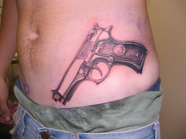 Tatuaje de pistola en el abdomen, como podemos observar esta pistola sí está acabada, pero al otro lado del abdomen se está iniciando también el tatuaje de una pistola del mismo tipo, la verdad es que, como venimos diciendo, es una moda muy extendida en los últimos años y que seguro llama la atención de la gente y de la policía también