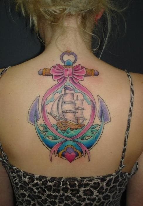 Tatuaje muy femenino y muy bonito de un ancla envuelto en un lazo rosa y en cuyo interior se ha dibujado un gran barco de vela al que no le faltan apenas detalles, incluidas las nubes, el cielo, la bandera del barco y el agua por el que navegar este bonito tattoo