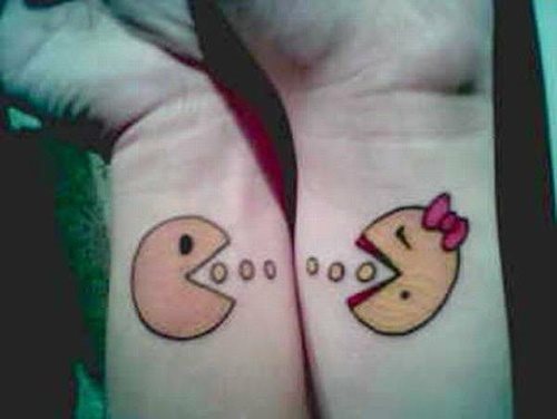 Tatuaje de pareja caracterizado por dos muñecos come cocos, en el que el chico se ha tatuado un comecoco y la chica otro, pero con lazo, los labios puntados y un pequeño lunar, el tatuaje se une porque ambos están comiendo