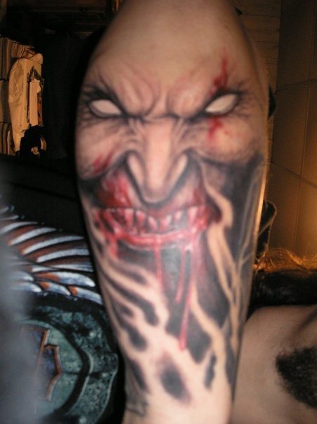 Tatuaje en el antebrazo de un vampiro con ojos blancos y dientes manchados de sangre, de cuya boca sale más sangre y al que se le ha ido tatuando una barba con sombreados que dan aspecto de continuidad a todo el tattoo