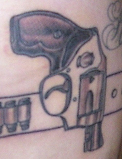 Tatuaje de un pequeño revolver sobre un cinturón con balas, es un tatuaje que a priori no nos gusta demasiado, pero que si decidiera dalr un poco de color y tatuar algunos detalles más relacionado con el mundo de las armas, nos gustaría algo más