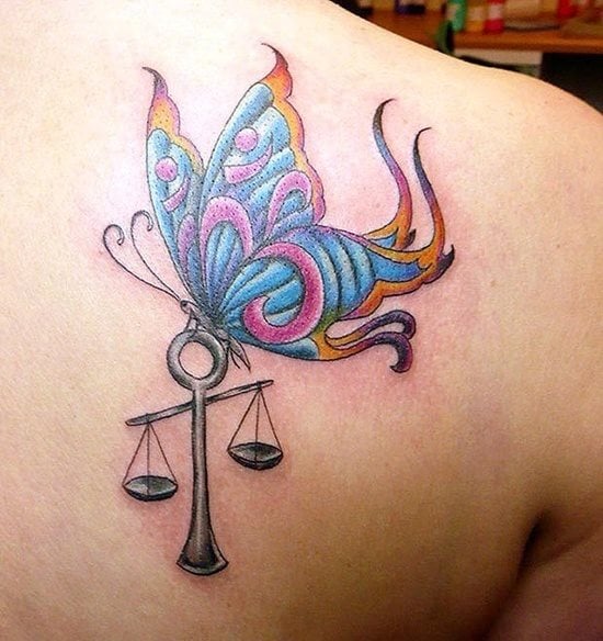 Tatuaje de una mariposa con bolitos colores y perfectos acabados que está posada sobre una balanza, este elemento de la balanza tiene un gran significado en el ámbito de la justicia, que viene a representar el equilibrio de la balanza entre verdad y justicia