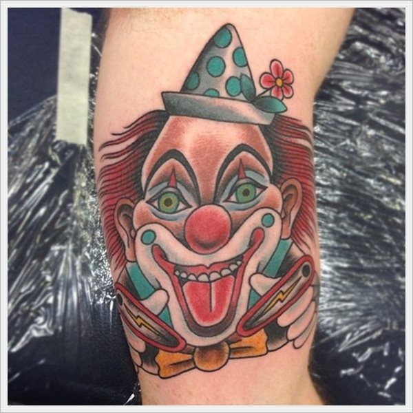 Divertido tattoo de un alegre payaso y muy colorido en el que destacan la gran sonrisa los ojos verdes, el sombrero de lunares con una margarita y que sin duda, de las partes que más nos gustan es el pelo rojo tan bien conjugado en la piel y las dos piezas de pinball que el payaso lleva en las manos, un detalle muy divertido y diferente para este tatuaje de payaso