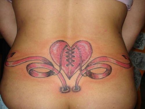 Tatuaje de un corazón de color rosa en la cintura acompañado por un lazo que hace las veces de cenefas del mismo color nos gusta el detalle del entrelazado del corazón y de que los lazos parezcan que salen del propio interior del cuerpo de esta chica