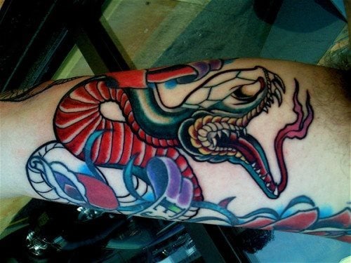 Llamativos tonos los de esta serpiente tatuada en el brazo y a la que acompaan otros motivos que no podemos apreciar correctamente