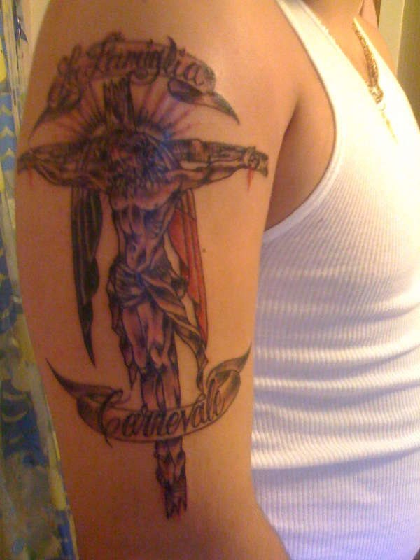 Tatuaje de Cristo crucificado y al que se le ha puesto una sábana en la cruz que le da un aire de alas, a este tatuaje se le han añadido las palabras La famiglia Carnevale o algo parecido, ya que no podemos identificar bien las palabras al no estar tatuadas con gran destreza