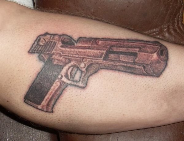 Tatuaje de una pistola descargada o a punto de ser montada sobre el antebrazo de un hombre, tatuaje poco original el de una pistola, pero que en esta ocasión se le ha dado un toque de originalidad al mostrarla a punto de ser montada