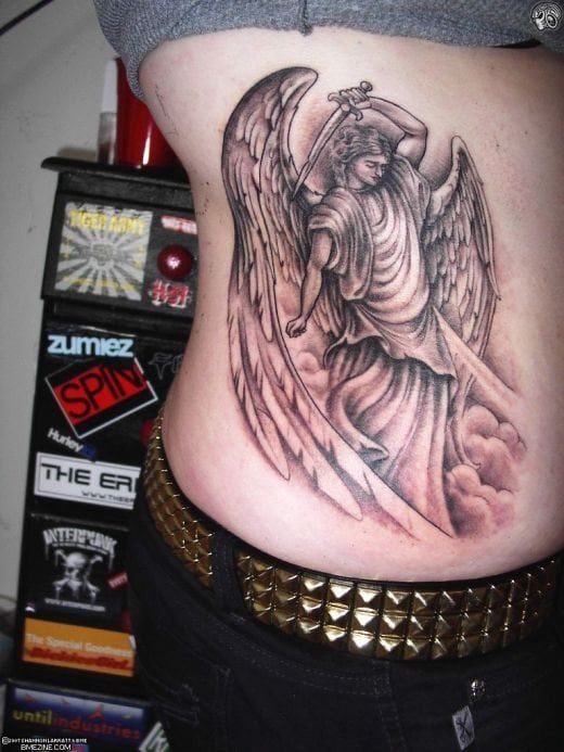 Tatuaje de un ángel guerrero al que se le ha vestido con una gran túnica y colocado una espada sobre la mano izquierda, el tatuaje como podemos ver, tiene unas grandes alas, casi más grandes que el propio cuerpo del ángel