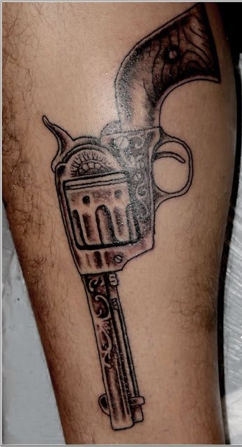 Gran tatuaje de un revolver sobre la pierna de un hombre, tatuaje para el que se han diseñado grandes detalles de la pistola, desde el cañón tallado, hasta las sombras del cargador y la culata de madera con el tornillo que llevan todos estos tipos de pistolas