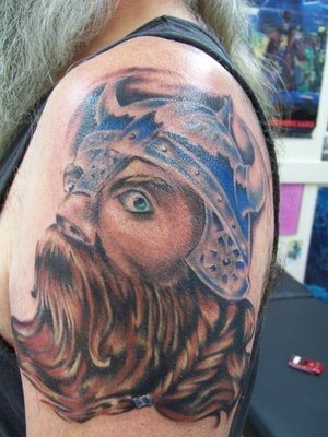 Un vikingo en la parte del brazo con colorido, pero con elementos que resultan extraos: el casco es muy pequeo, no tiene boca, 
