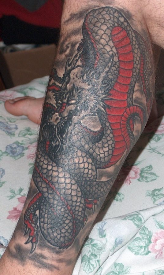 Este hombre se ha tatuado en la pierna un enorme dragón de color negro y partes rojas, al que ha añadido un gran fondo sombreado negro que cubre casi la totalidad de su pierna, un tattoo muy vistoso y bonito