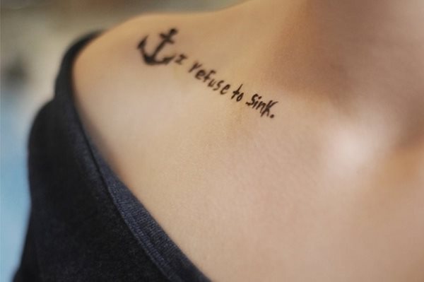 Tatuaje de un pequeño ancla en la parte delantera del hombro, seguido por la frase 