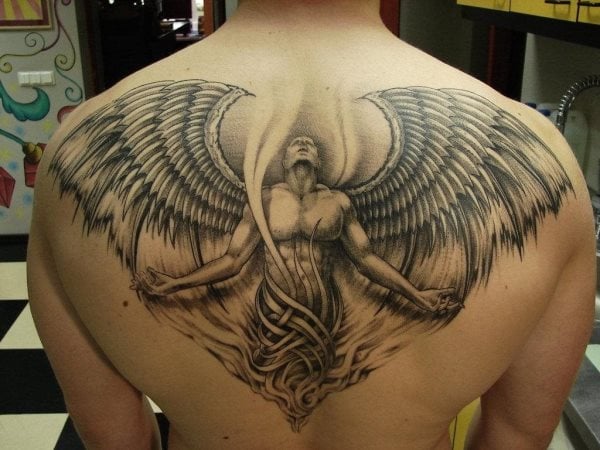 Tatuaje de un espectacular ángel con los brazos abiertos hacia el cielo, al igual que su mirada, envuelto por unos tribales que hacen las beces de la túnica y unas imponentes alas que ocupan toda la espalda del cuerpo de este hombre